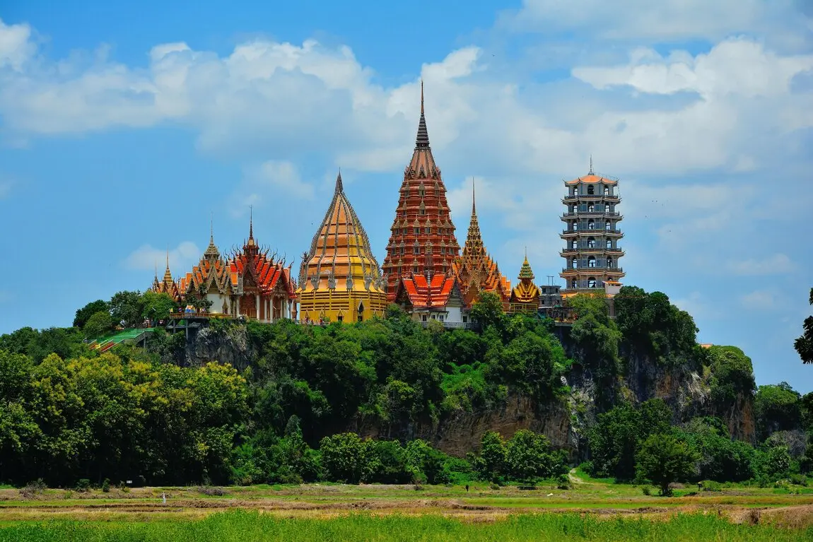 Auf einem Berg steht ein Tempel in Thailand, umgeben von grüneWäldern und Wiesen.